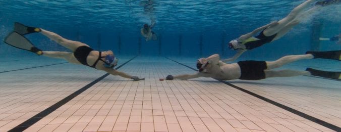 Two underwater hockey players reaching for the puck